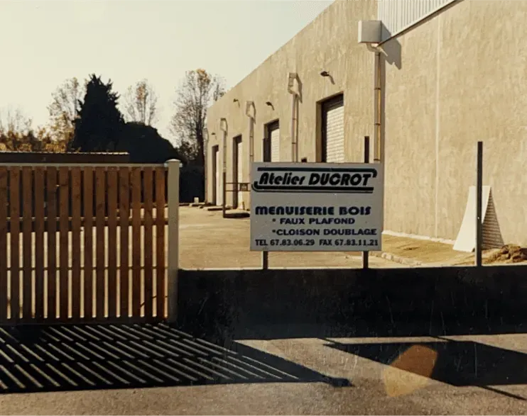 Façade des Ateliers Ducrot : panneau enseigne, portail en bois et ciel bleu ensoleillé.
