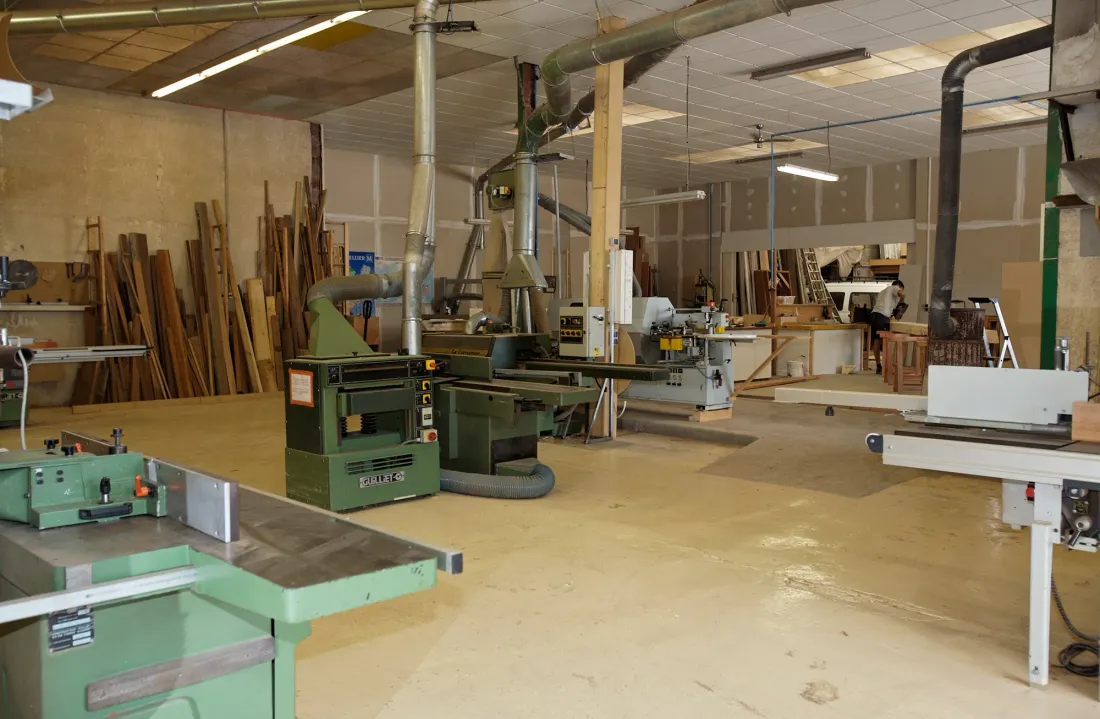 Atelier de menuiserie de Lunel : machines à bois vertes, stocks de planches, aspiration et établis.