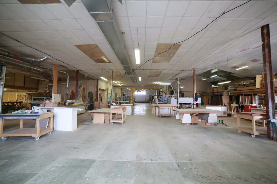 L'atelier bois de Lunel : établis, panneaux et machines alignés sous l'éclairage de la halle