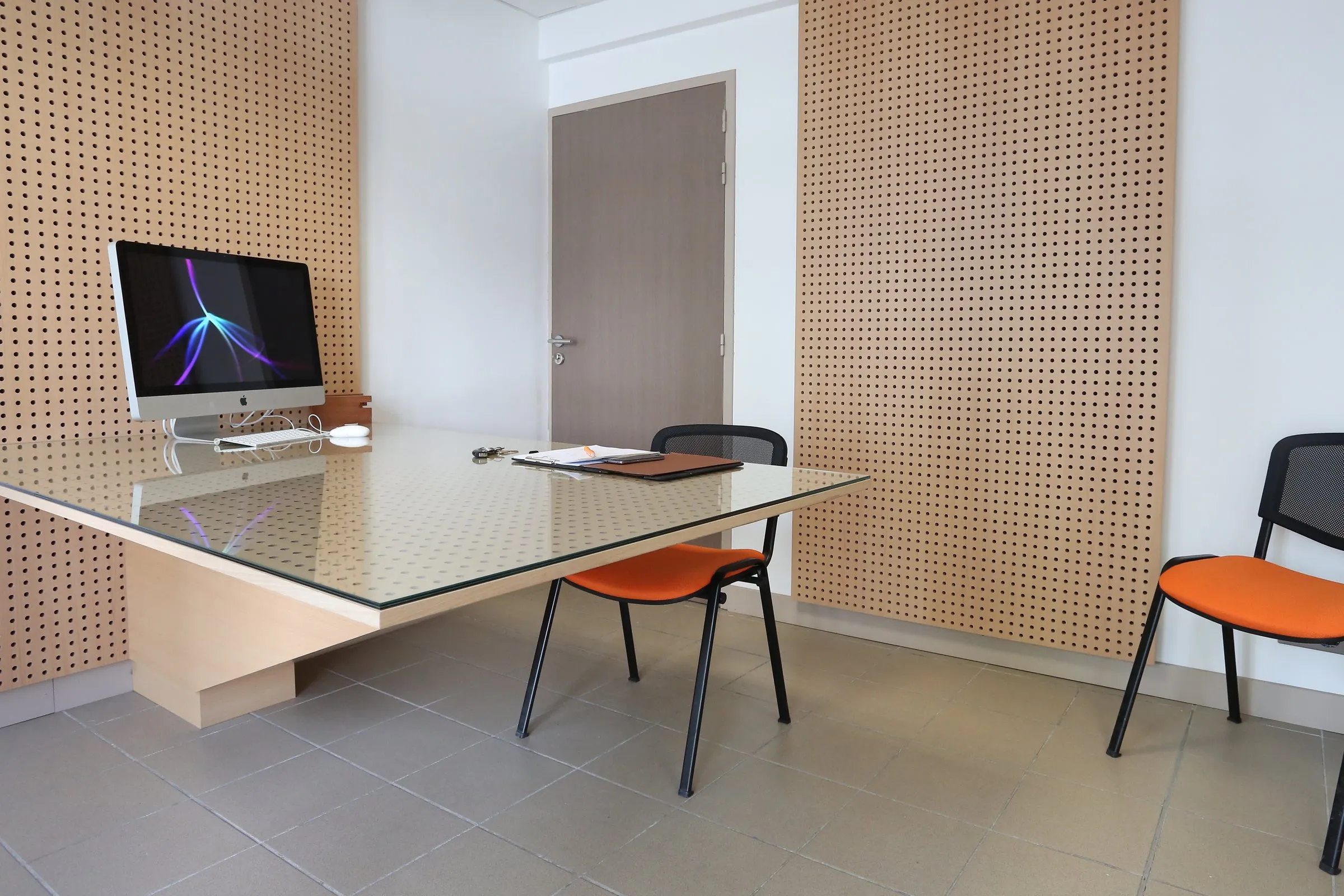 Bureau à plateau de verre sur piètement bois, murs en panneaux perforés