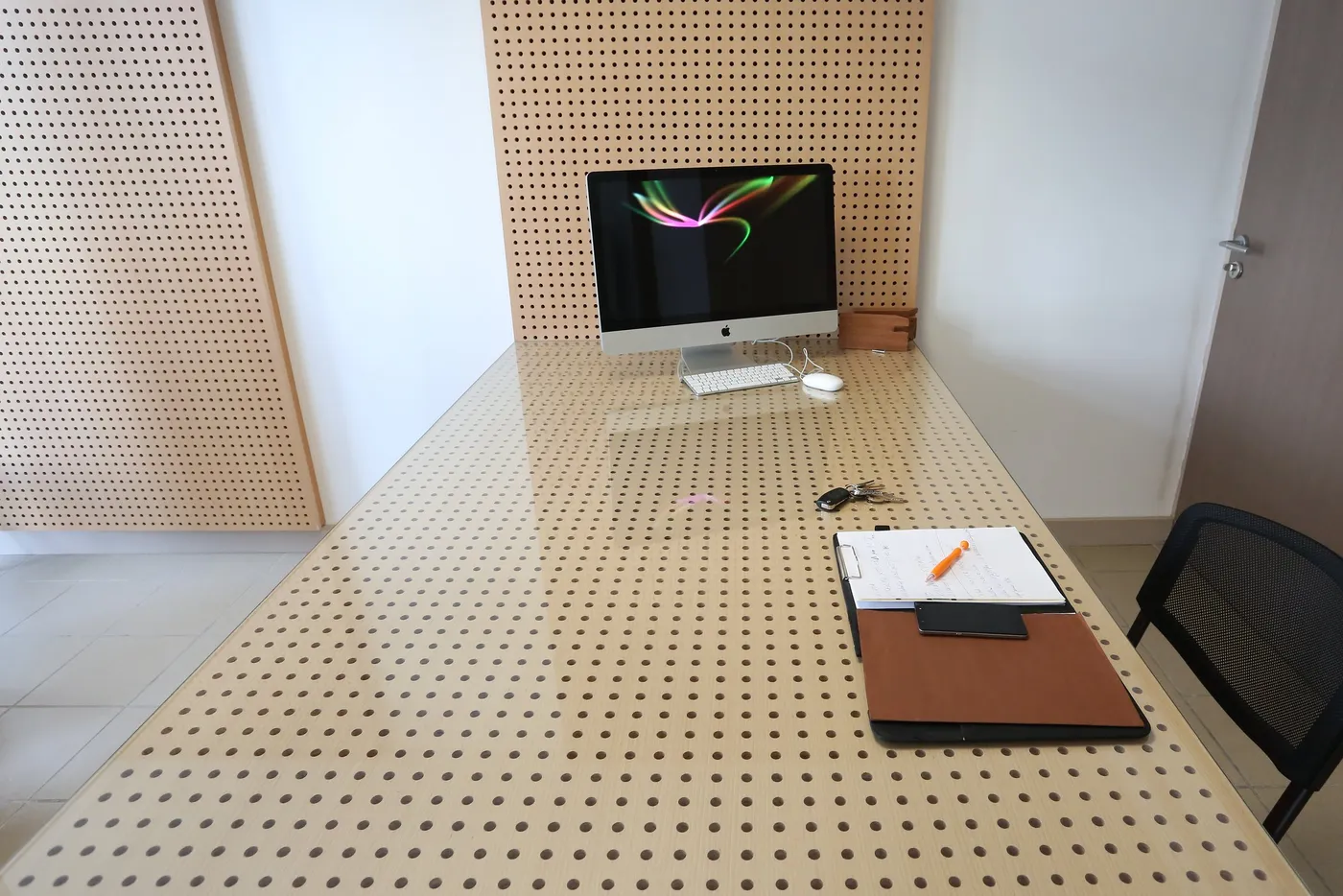 Grande table à plateau perforé devant un mur habillé de panneaux de bois perforés