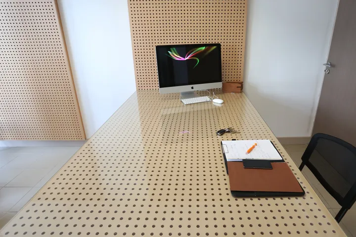 Grande table à plateau perforé devant un mur habillé de panneaux de bois perforés
