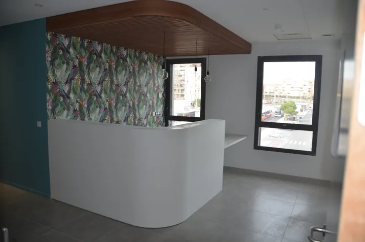 Banque d'accueil courbe blanche sous un plafond à lamelles bois, cabinet médical à Montpellier