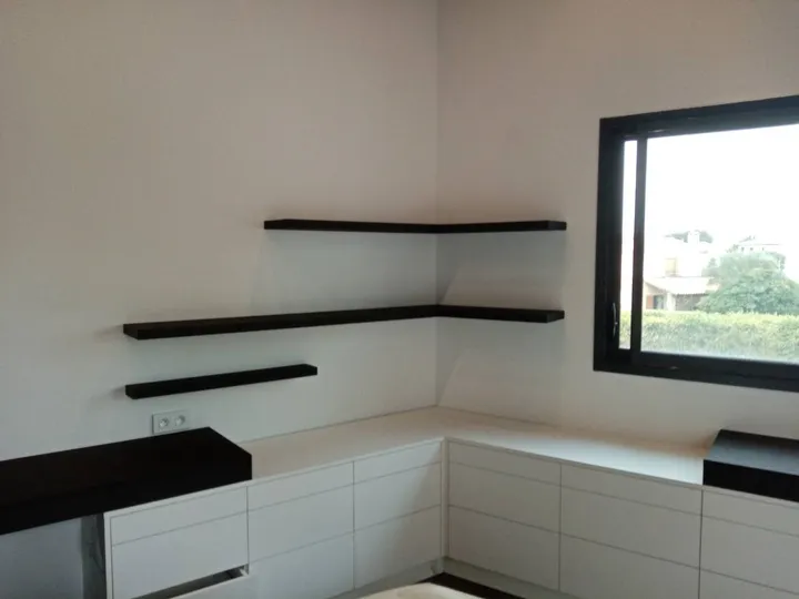 Tiroirs blancs sans poignée et étagères flottantes noires dans l'angle d'une chambre