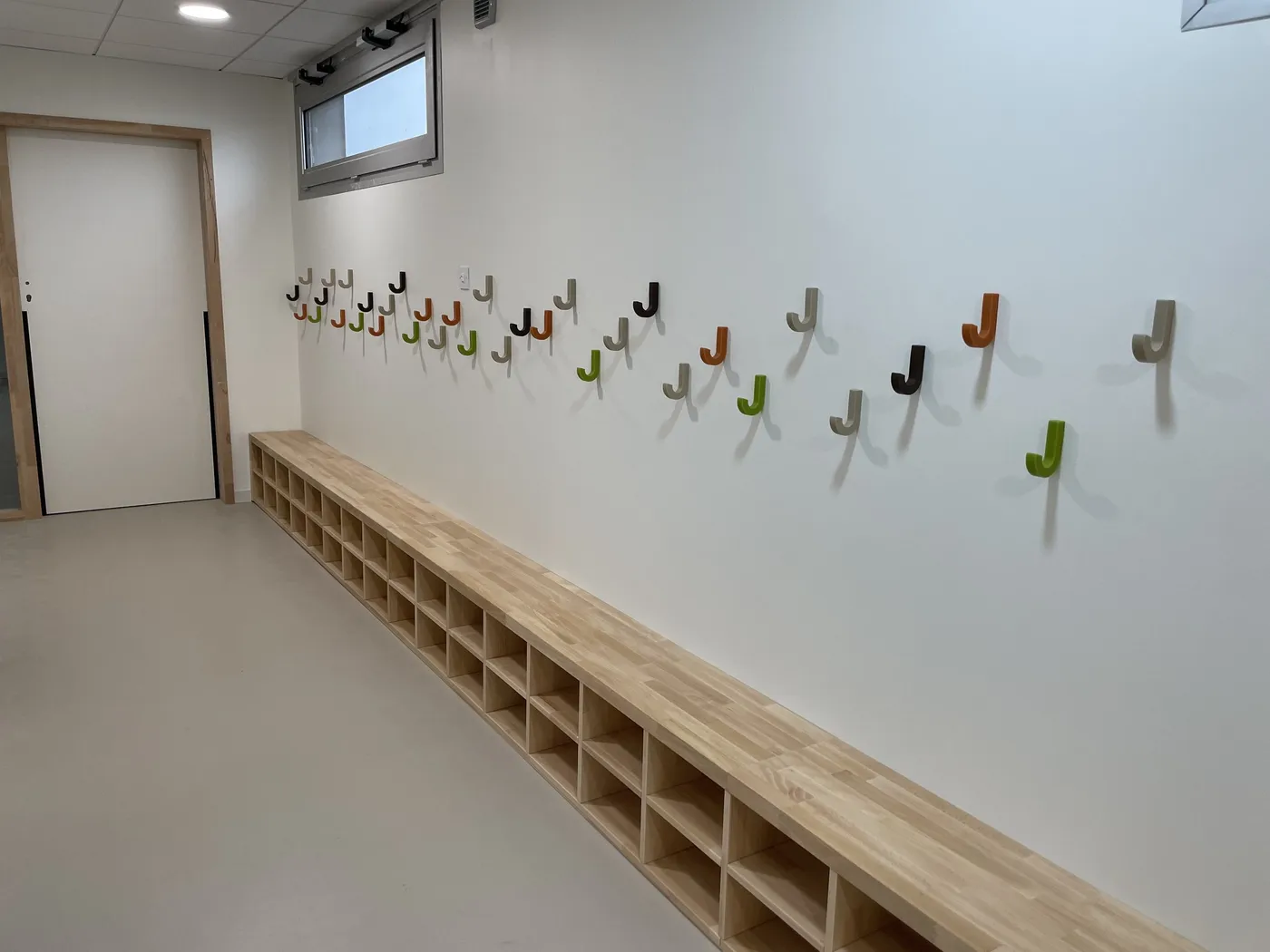 Banc-vestiaire à casiers et patères colorées dans le couloir d'une école