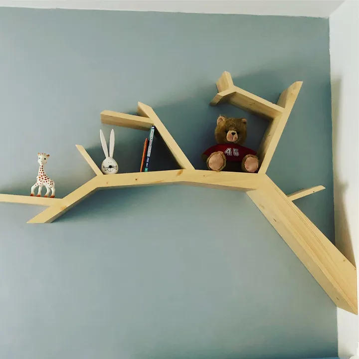 Étagère murale en forme d'arbre en bois clair, sur un mur bleu de chambre d'enfant