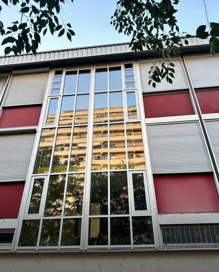 Mur-rideau aluminium toute hauteur entre les volets roulants et les panneaux rouges de la façade