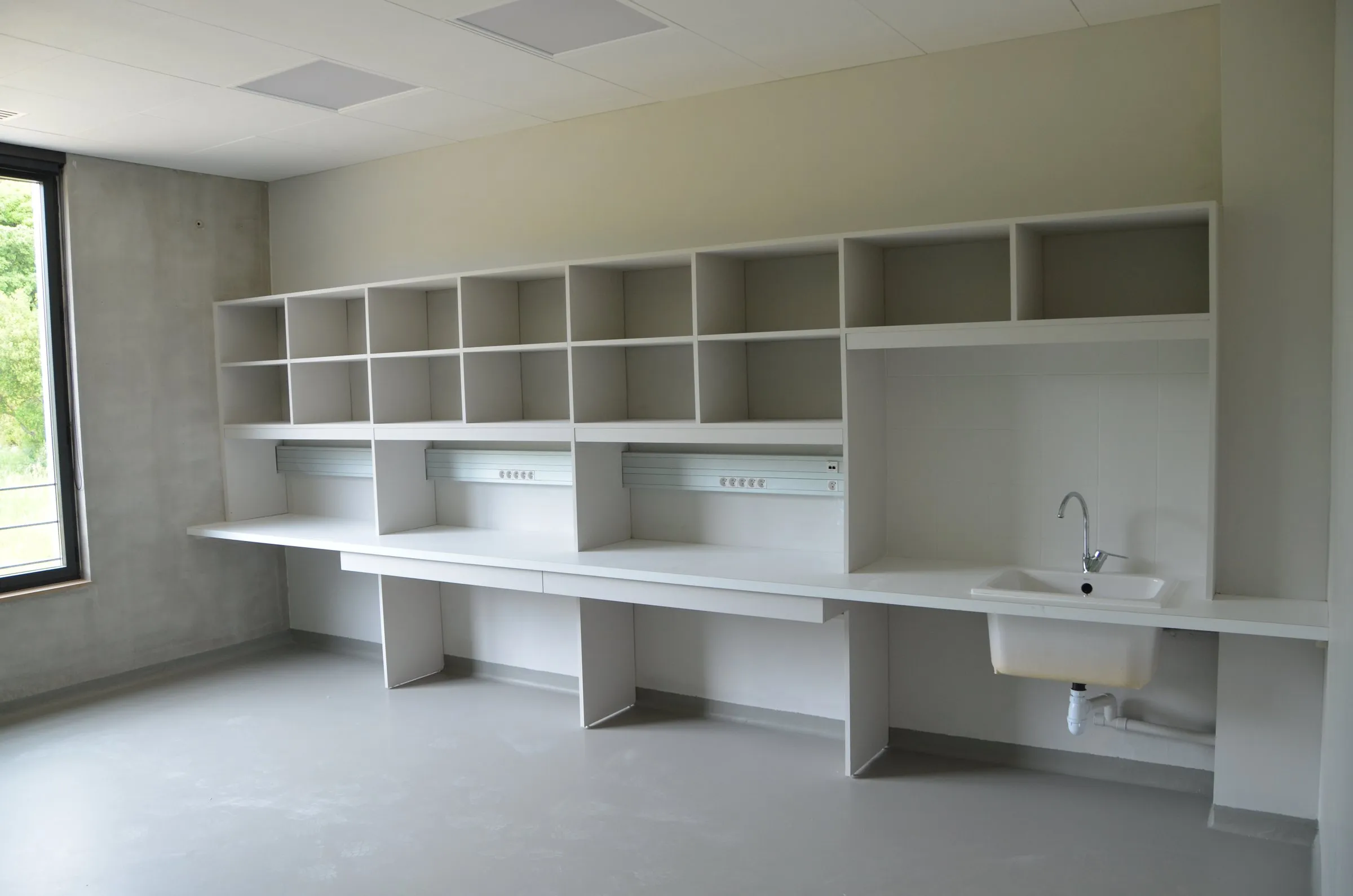 Salle de travaux pratiques, longue paillasse blanche et casiers hauts
