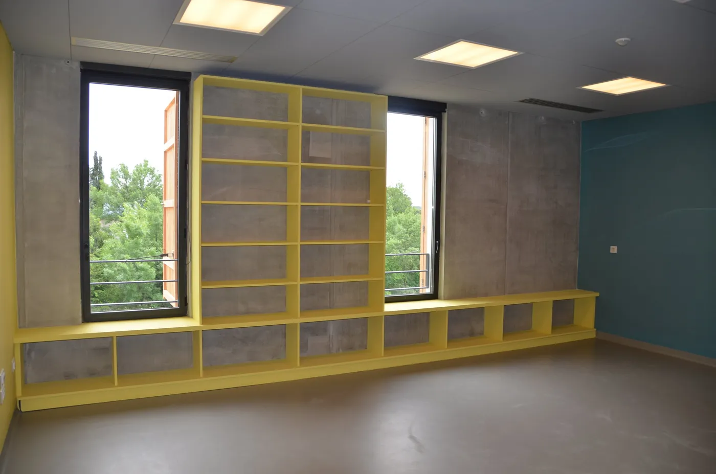 Bibliothèque jaune sur mesure et banquette sous la fenêtre dans une salle d'école