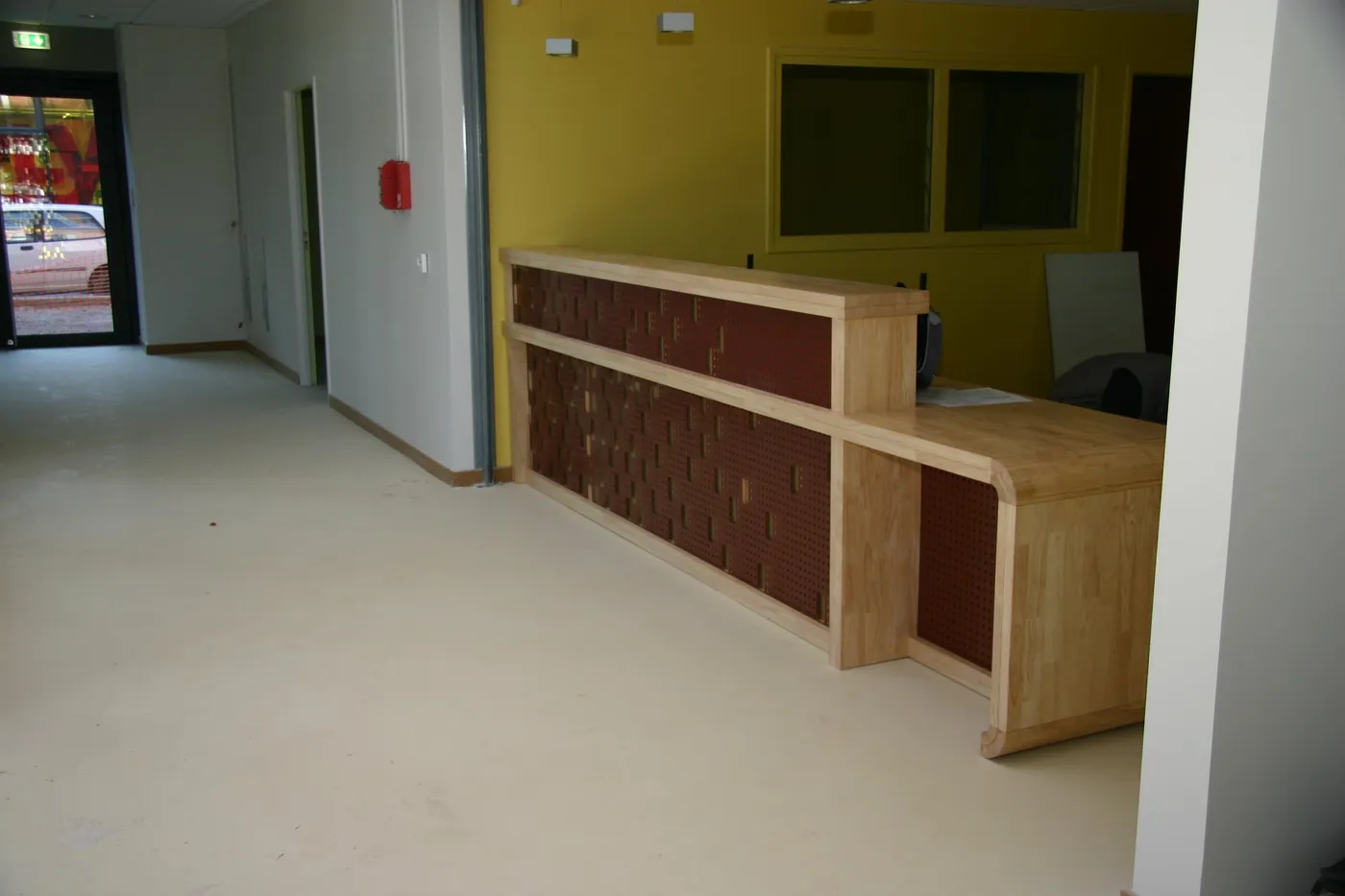 Banque d'accueil en bois clair à panneaux rouges motifs, dans un hall aux murs jaunes