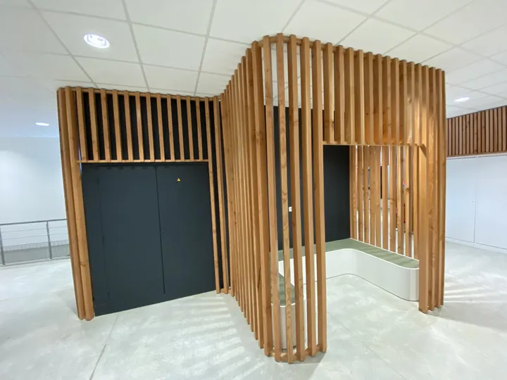 Claustra en lames de bois verticales et banc intégré dans le hall d'un lycée à Montpellier