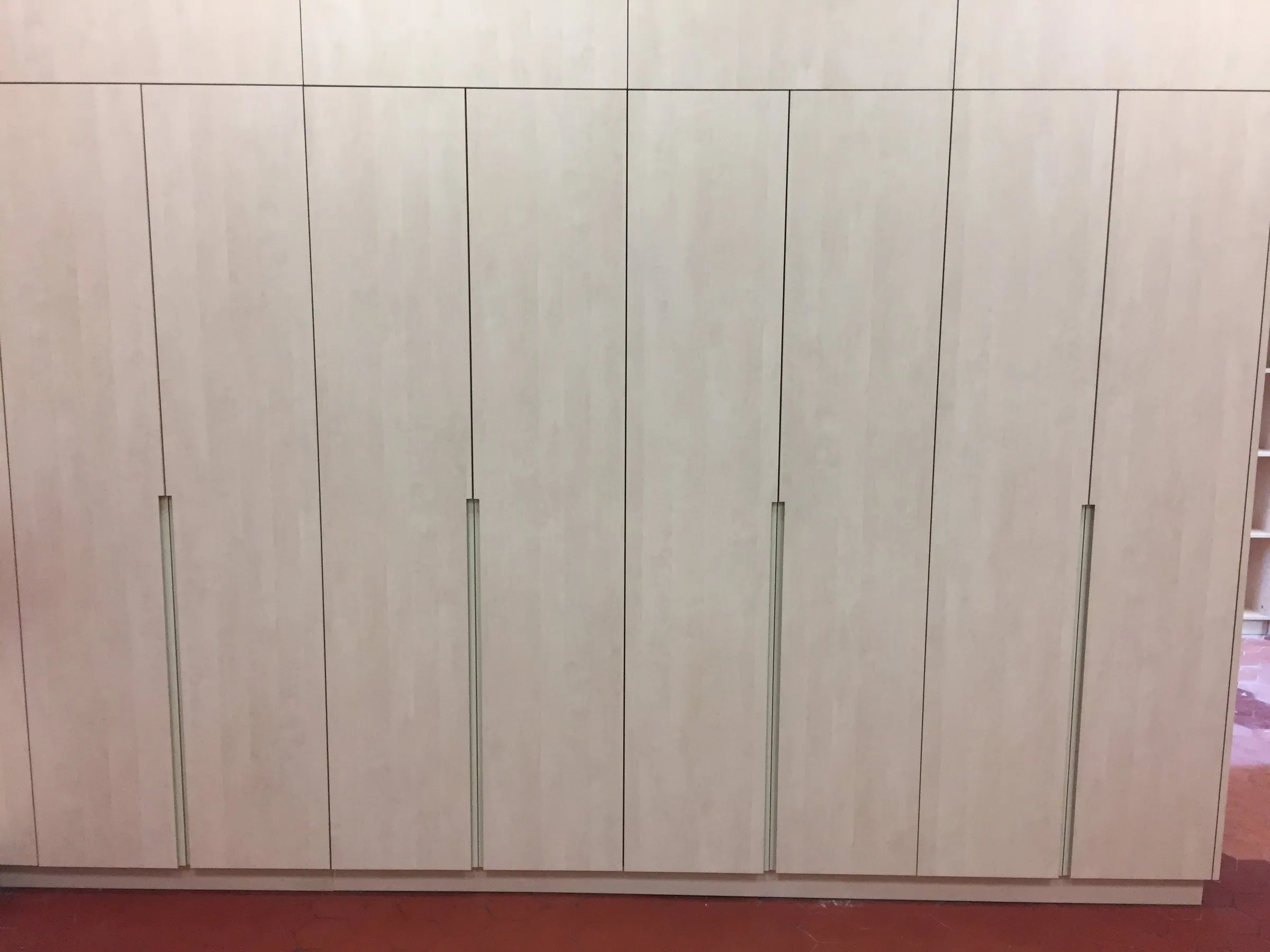 Mur de placards en bois clair à poignées intégrées