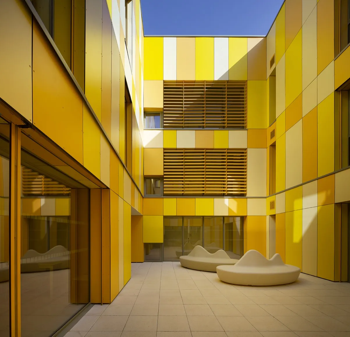 Patio intérieur habillé de panneaux de façade en camaïeu de jaunes, brise-soleil orientables sur deux niveaux