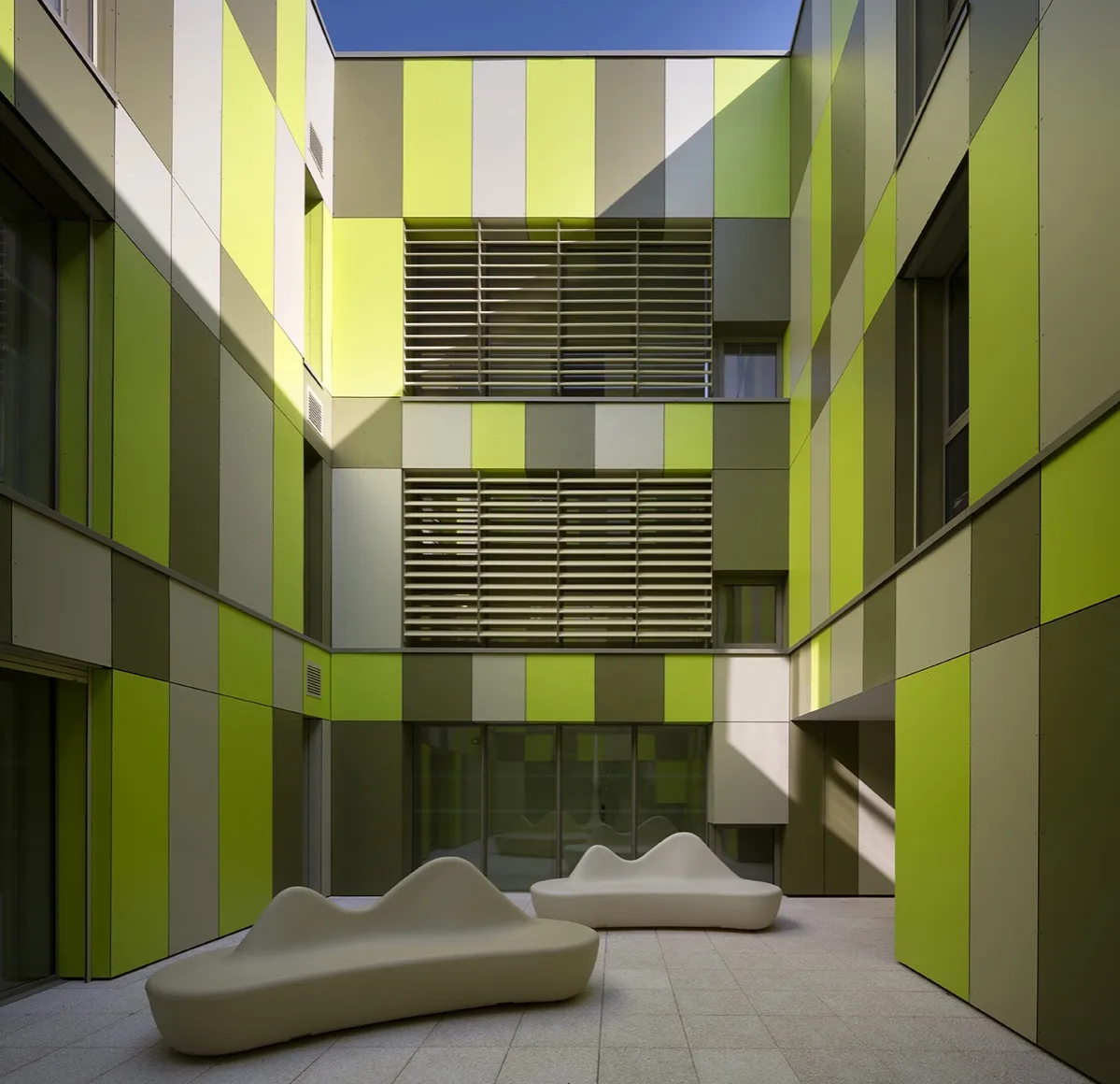 Patio intérieur habillé de panneaux de façade en camaïeu de verts, brise-soleil orientables sur deux niveaux