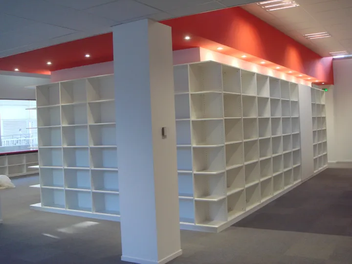Murs de casiers blancs sous un bandeau rouge sur un plateau de bureaux