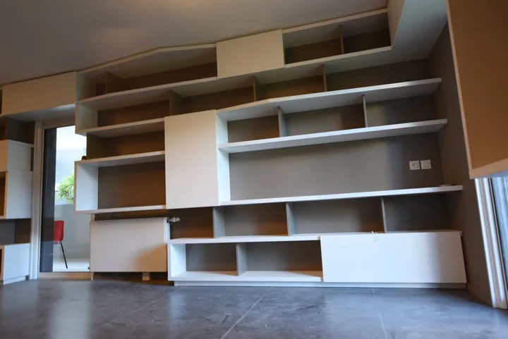 Grand mur de bibliothèques asymétriques et rangements sur mesure dans le séjour d'une villa
