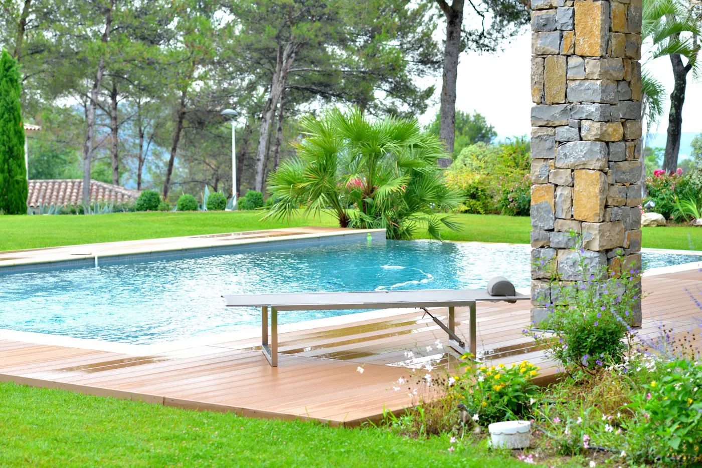 Terrasse en lames de bois autour d'une piscine, jardin et pins